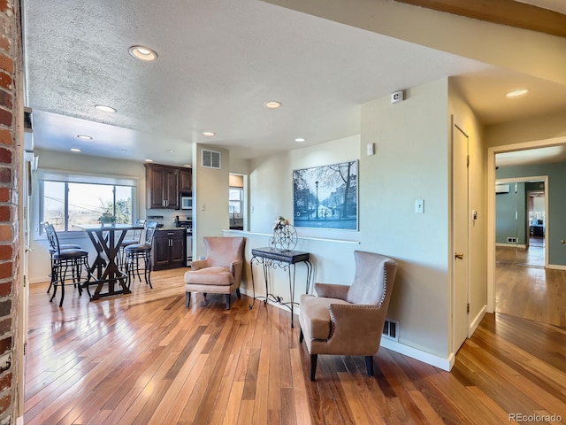 living area with a wall mounted air conditioner, a textured ceiling, and light hardwood / wood-style flooring