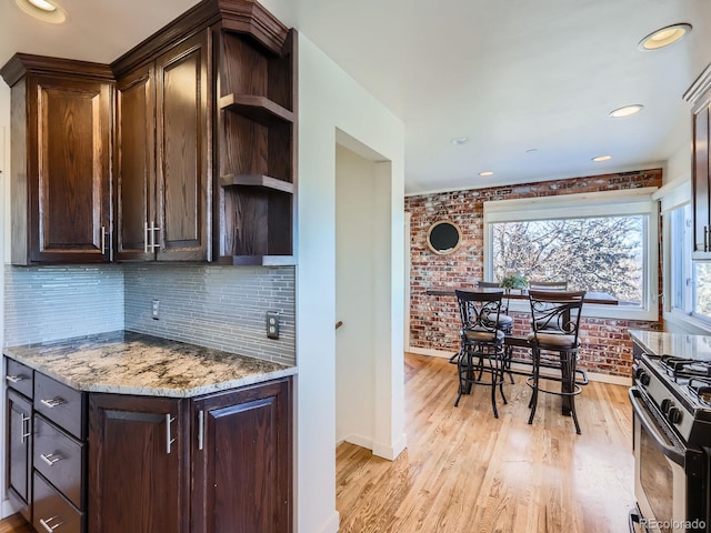 kitchen featuring light stone countertops, dark brown cabinets, stainless steel range with gas cooktop, and light hardwood / wood-style floors