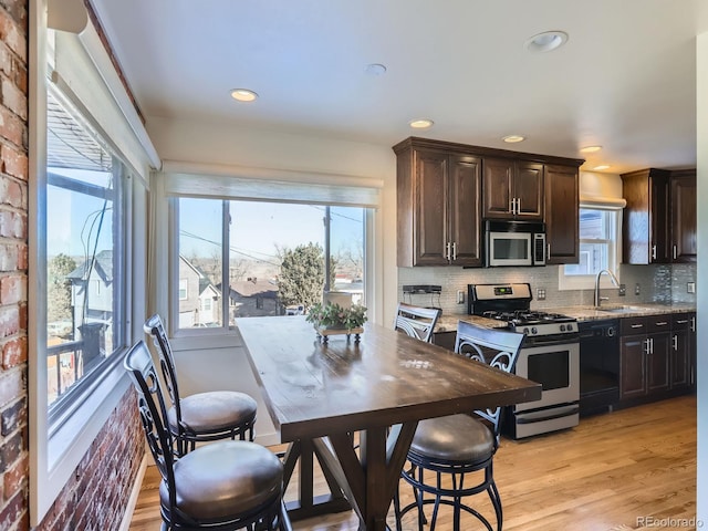 kitchen with light hardwood / wood-style floors, stainless steel appliances, dark brown cabinets, light stone counters, and sink