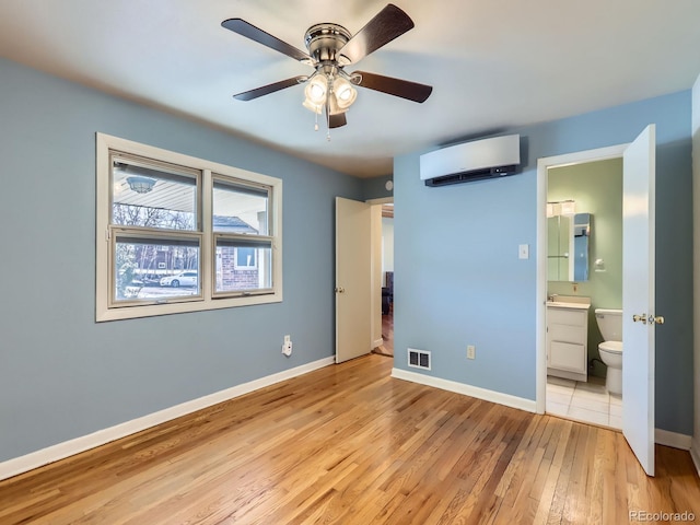 unfurnished bedroom featuring ceiling fan, ensuite bath, light hardwood / wood-style flooring, an AC wall unit, and sink