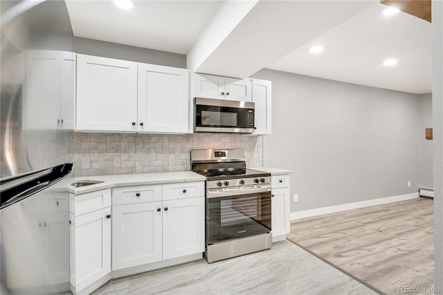 kitchen with baseboard heating, appliances with stainless steel finishes, tasteful backsplash, and white cabinetry