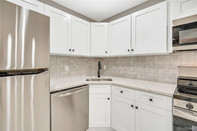 kitchen featuring stainless steel appliances, light stone counters, sink, white cabinetry, and tasteful backsplash