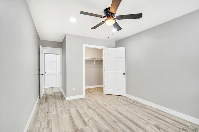 unfurnished bedroom with ceiling fan, a walk in closet, light wood-type flooring, and a closet