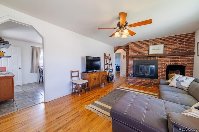 living room featuring light wood-type flooring, a ceiling fan, arched walkways, and a fireplace