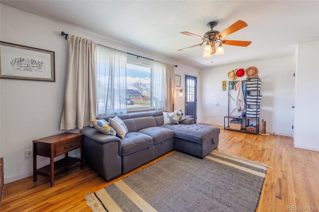 living room featuring a ceiling fan, baseboards, and light wood-type flooring