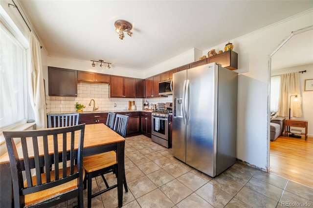kitchen with light tile patterned flooring, light stone counters, a sink, appliances with stainless steel finishes, and backsplash