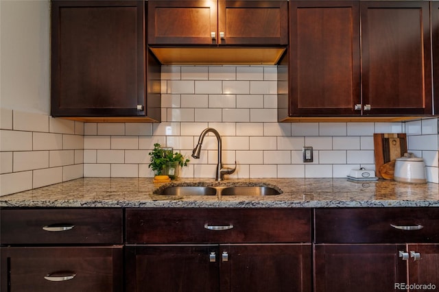 kitchen featuring light stone counters, a sink, decorative backsplash, and dark brown cabinetry