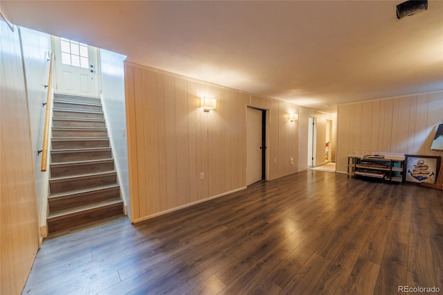 unfurnished living room featuring wood-type flooring, wood walls, and stairway