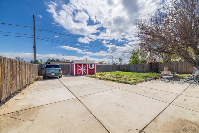 view of patio featuring a storage shed, driveway, an outbuilding, and a fenced backyard