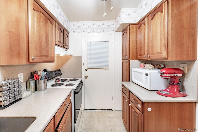 kitchen with under cabinet range hood, range with electric cooktop, white microwave, and light countertops