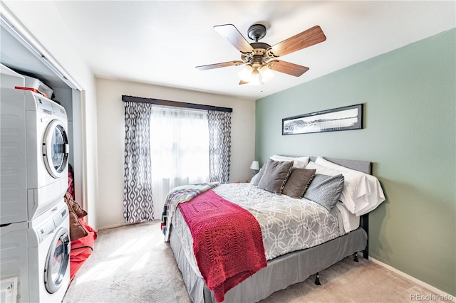 carpeted bedroom featuring stacked washing maching and dryer, a ceiling fan, and baseboards