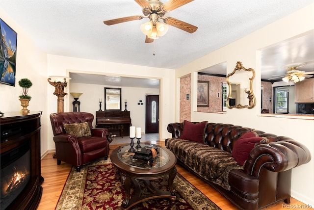 5215 S Washington St, Littleton, CO 80121 - living room featuring ceiling fan, light wood-style floors, a glass covered fireplace, and a textured ceiling