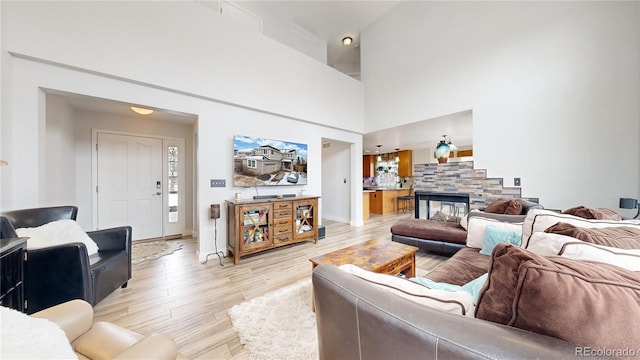 living room with a stone fireplace, a towering ceiling, and light wood-type flooring