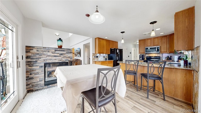 kitchen featuring decorative light fixtures, black refrigerator with ice dispenser, light hardwood / wood-style flooring, electric range, and a fireplace