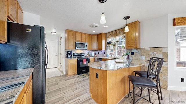 kitchen featuring pendant lighting, black appliances, a kitchen breakfast bar, kitchen peninsula, and light hardwood / wood-style flooring