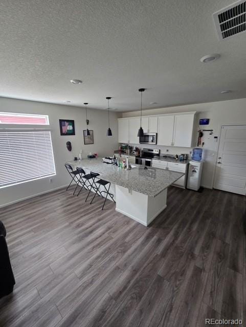 18006 E 103rd Ave, Commerce City, CO 80022 - kitchen featuring appliances with stainless steel finishes, a textured ceiling, a breakfast bar, white cabinetry, and dark wood finished floors