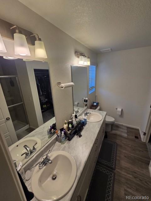 18006 E 103rd Ave, Commerce City, CO 80022 - bathroom featuring a stall shower, a textured ceiling, double vanity, wood finished floors, and toilet