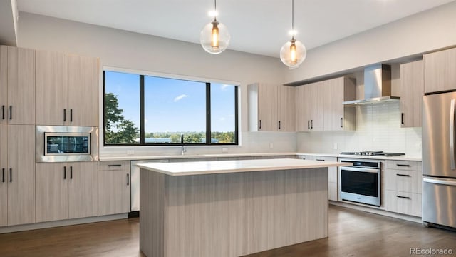 kitchen with decorative light fixtures, wall chimney exhaust hood, stainless steel appliances, and a kitchen island