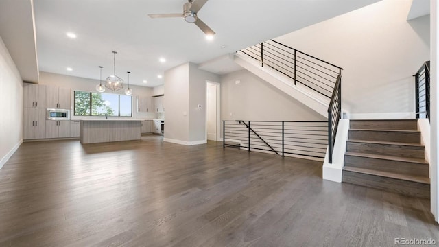 unfurnished living room featuring ceiling fan with notable chandelier and dark wood-type flooring