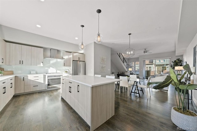 kitchen featuring a center island, wall chimney exhaust hood, decorative light fixtures, stainless steel fridge, and stove