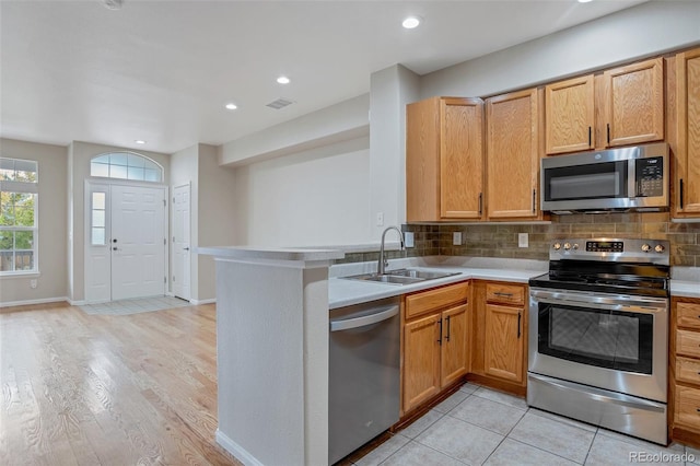 kitchen featuring kitchen peninsula, backsplash, stainless steel appliances, sink, and light hardwood / wood-style flooring