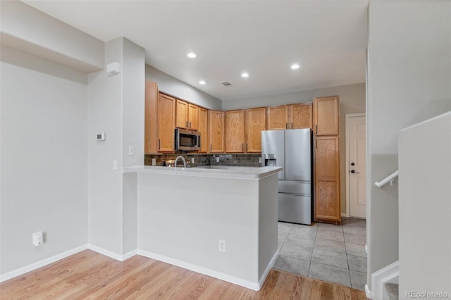 kitchen featuring sink, decorative backsplash, light wood-type flooring, kitchen peninsula, and stainless steel appliances