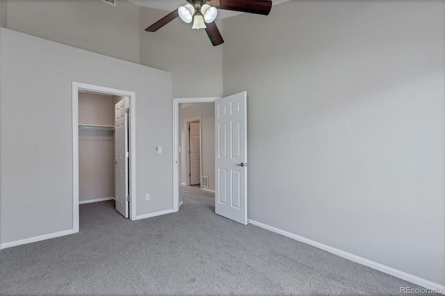 unfurnished bedroom featuring carpet, a high ceiling, a walk in closet, ceiling fan, and a closet