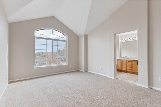 unfurnished bedroom featuring vaulted ceiling, light colored carpet, sink, and ensuite bath