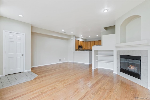 unfurnished living room with light hardwood / wood-style flooring and a tiled fireplace