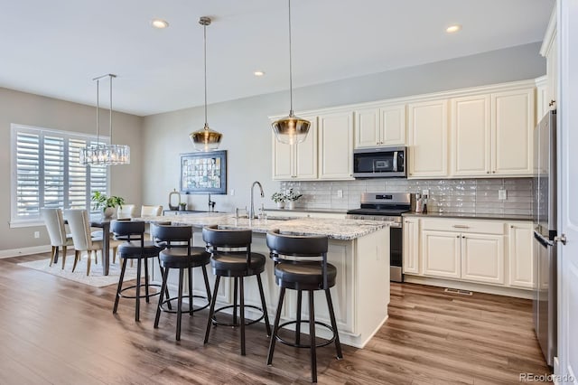 268 Simmental Loop, Castle Rock, CO 80104 - kitchen featuring appliances with stainless steel finishes, decorative backsplash, wood finished floors, an island with sink, and a kitchen breakfast bar