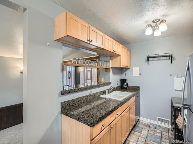 kitchen featuring black dishwasher, sink, stainless steel fridge, light brown cabinets, and a textured ceiling