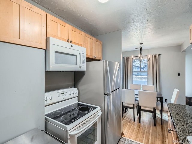 kitchen with light brown cabinetry, decorative light fixtures, a chandelier, dark stone counters, and white appliances