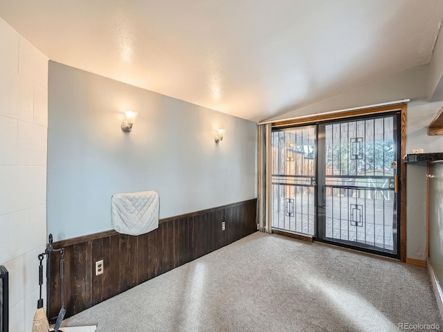 unfurnished room with lofted ceiling, wooden walls, and carpet