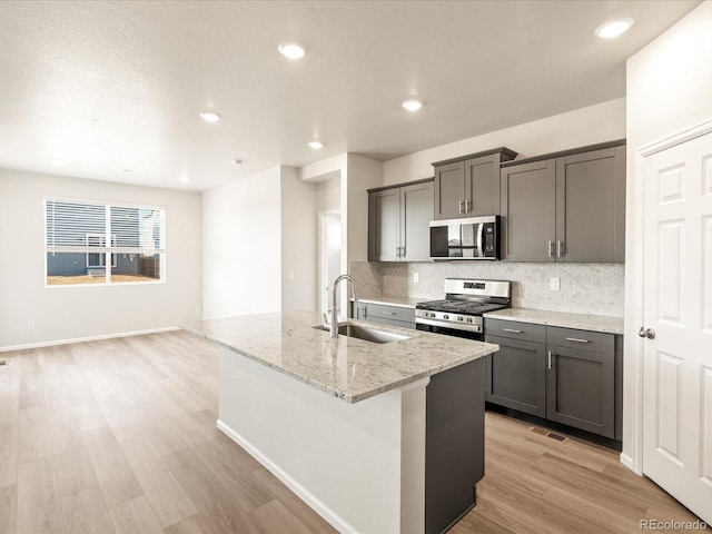 kitchen with sink, stainless steel appliances, light stone countertops, a center island with sink, and light hardwood / wood-style flooring