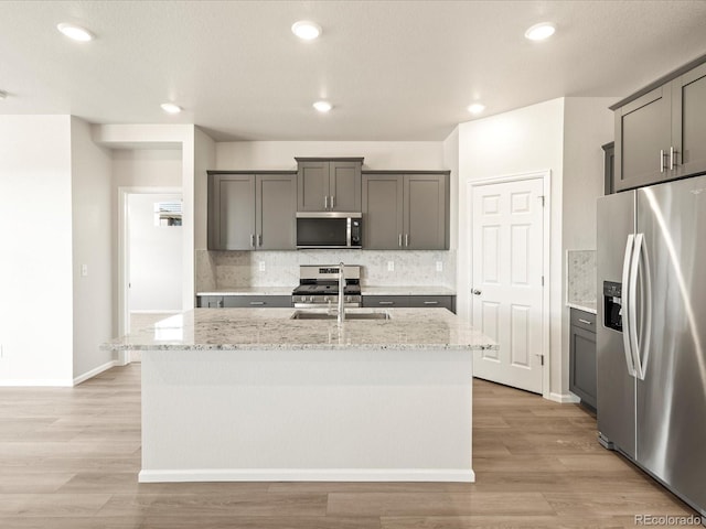 kitchen with gray cabinets, sink, a kitchen island with sink, stainless steel appliances, and light stone countertops