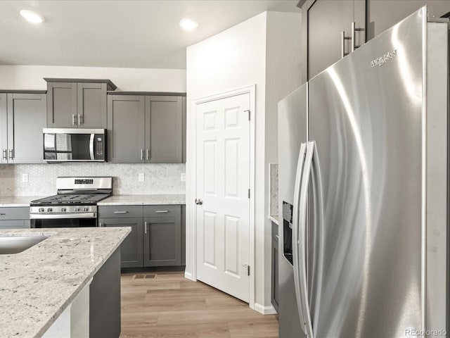 kitchen featuring tasteful backsplash, light hardwood / wood-style flooring, appliances with stainless steel finishes, gray cabinets, and light stone countertops