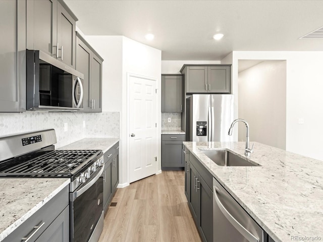 kitchen featuring sink, light hardwood / wood-style flooring, appliances with stainless steel finishes, light stone counters, and decorative backsplash