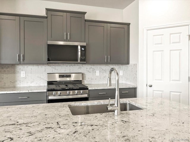 kitchen featuring light stone counters, backsplash, stainless steel appliances, and sink