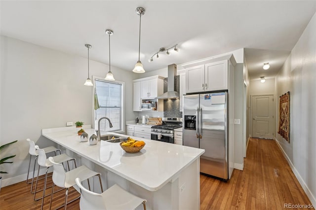 3444 Lawrence St, Denver, CO 80205 - kitchen with appliances with stainless steel finishes, a sink, wall chimney exhaust hood, a kitchen bar, and hardwood / wood-style floors