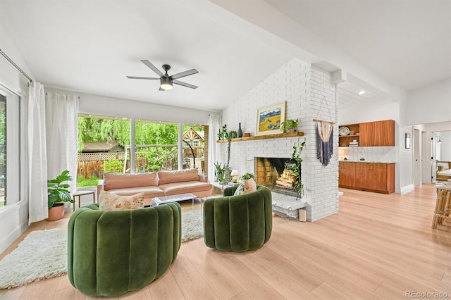 5200 W Rowland Ave, Littleton, CO 80128 - living room featuring vaulted ceiling, a ceiling fan, a brick fireplace, light wood-type flooring, and baseboards