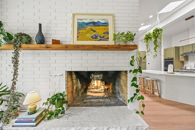 5200 W Rowland Ave, Littleton, CO 80128 - detailed view of under cabinet range hood, a brick fireplace, and wood finished floors