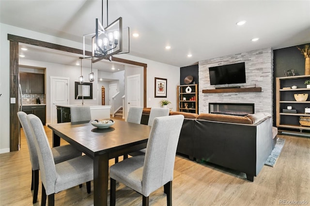 dining space featuring recessed lighting, light wood-style floors, a stone fireplace, and stairs