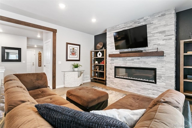 living area featuring visible vents, baseboards, a stone fireplace, recessed lighting, and wood finished floors