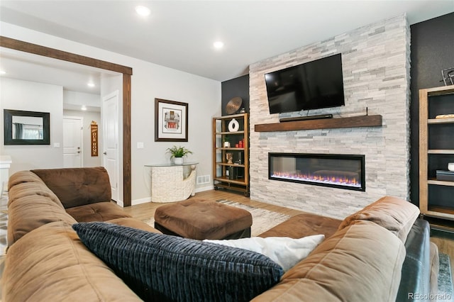 living area featuring wood finished floors, visible vents, baseboards, recessed lighting, and a stone fireplace