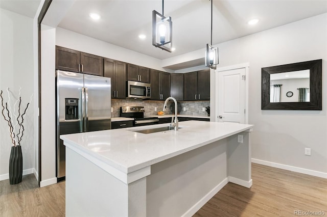 kitchen featuring backsplash, dark brown cabinets, appliances with stainless steel finishes, light wood-style floors, and a sink