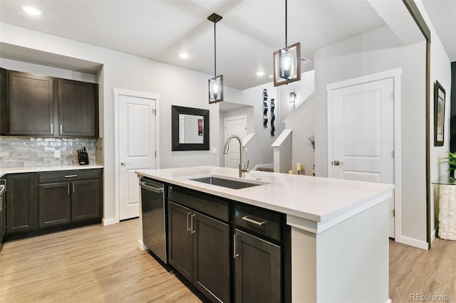 kitchen featuring light wood finished floors, a sink, decorative backsplash, stainless steel dishwasher, and decorative light fixtures