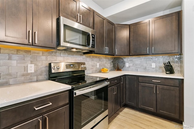 kitchen featuring dark brown cabinets, light stone counters, decorative backsplash, appliances with stainless steel finishes, and light wood-style floors