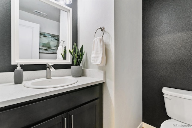 bathroom featuring visible vents, toilet, vanity, and a textured wall