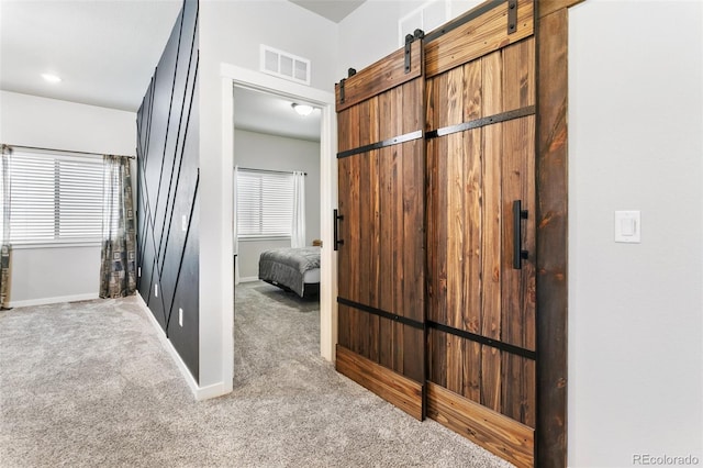 hall featuring visible vents, carpet flooring, baseboards, and a barn door