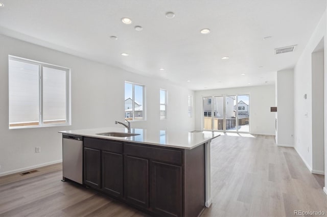 kitchen with a center island with sink, dark brown cabinets, stainless steel dishwasher, light hardwood / wood-style floors, and sink